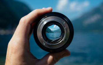 hand holding camera lens focusing on water and distant mountains