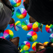 group looking up at colorful umbrellas strung together to span the gap between two buildings