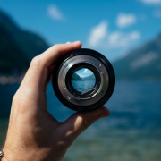 hand holding camera lens focusing on water and distant mountains